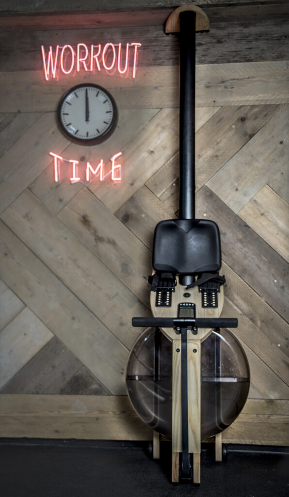 Hand-built wooden water rower in front of a chevron-pattern reclaimed timber wall