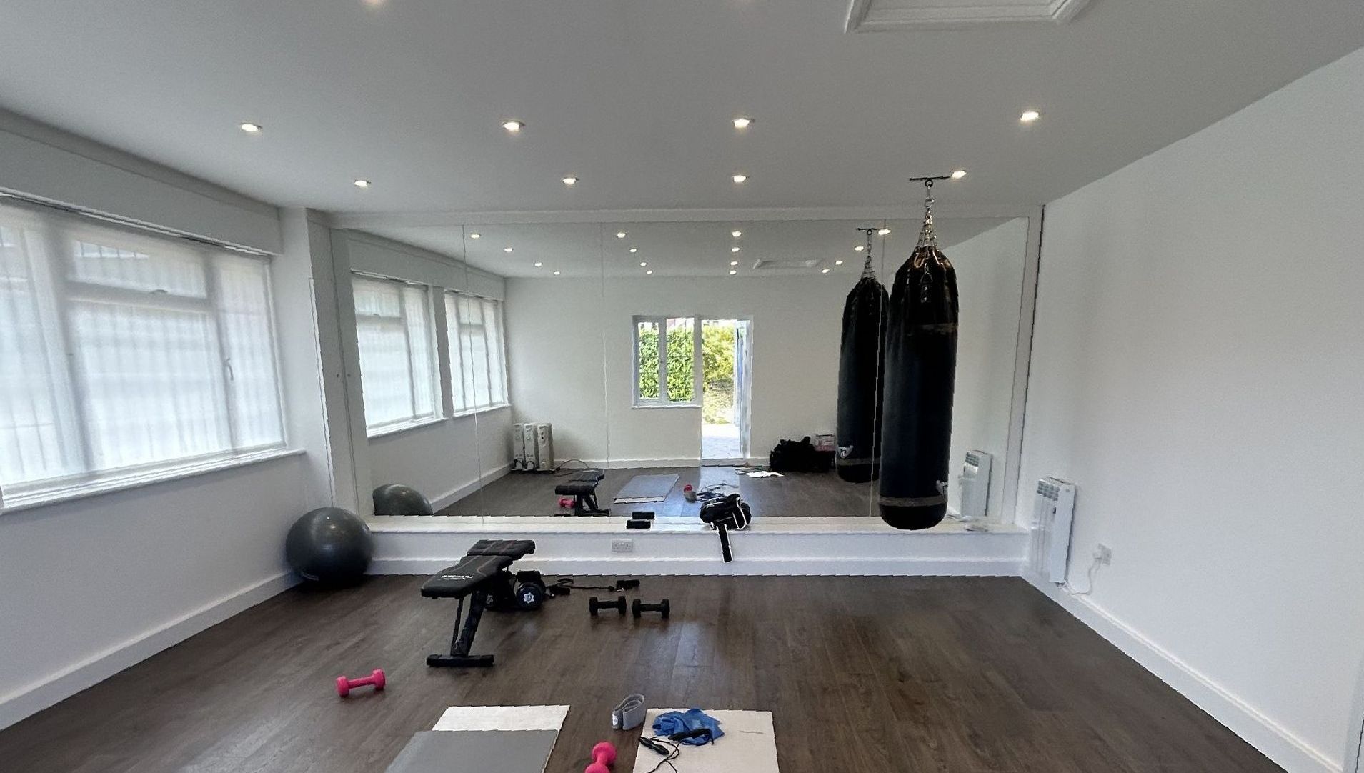 A home gym with white walls, mirrors, a hanging punch bag and basic equipment, before transformation.